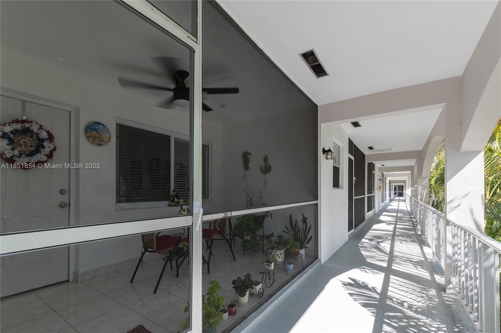 A screened-in balcony with a ceiling fan overlooks an outdoor walkway in an apartment complex — 581 Blue Heron Dr # B, Hallandale Beach FL 33009, HALLANDALE BEACH, FL