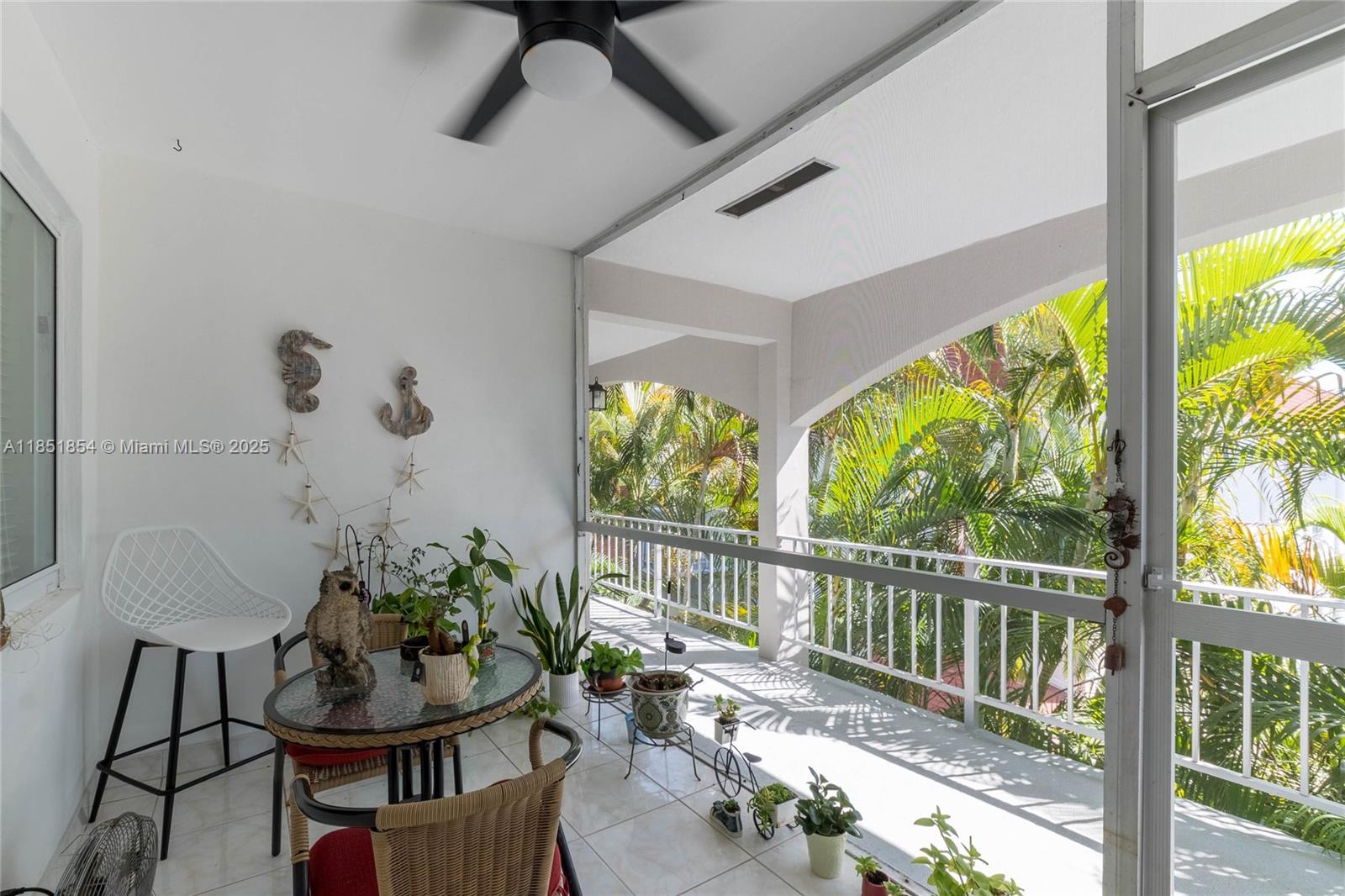 A covered balcony features a small dining set, potted plants, and a view of palm trees — 581 Blue Heron Dr # B, Hallandale Beach FL 33009, HALLANDALE BEACH, FL