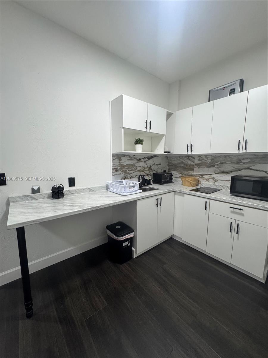 A kitchen features white cabinets, marble-patterned countertops, a backsplash, and dark wood-look flooring — 12959 SW 229th Ter # 0, Miami FL 33170, MIAMI, FL