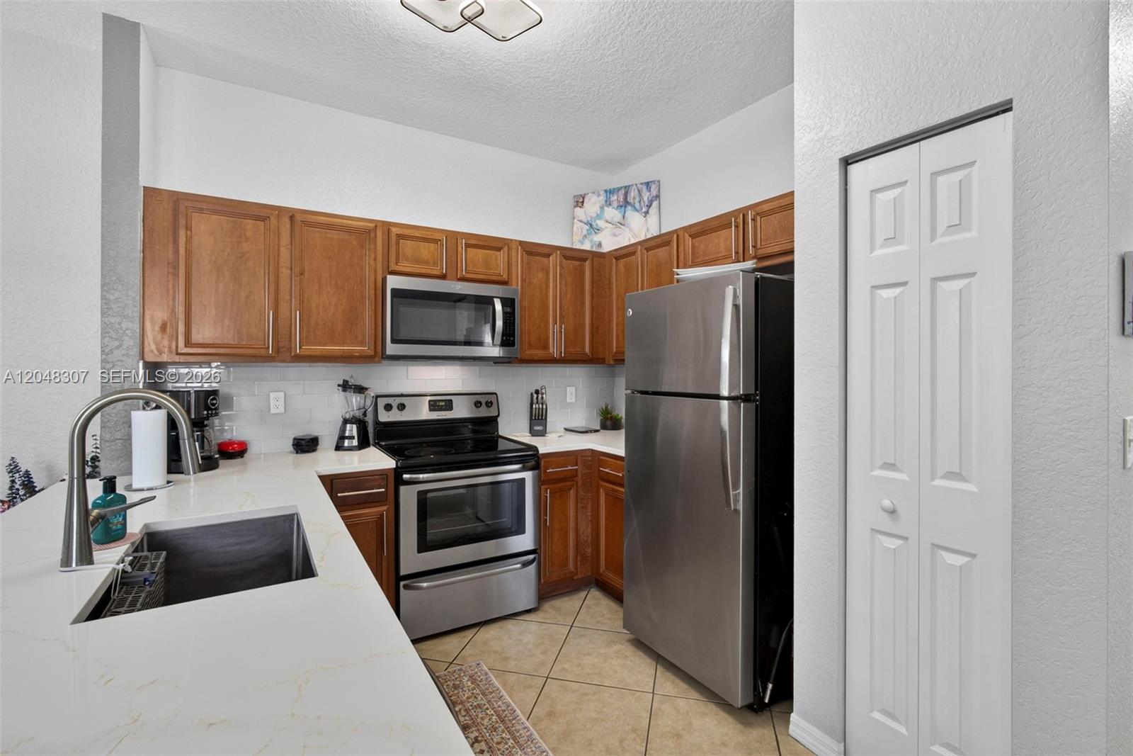 A kitchen features wooden cabinets, stainless steel appliances, and white countertops with a sink — 3107 Grandiflora Dr, Green Acres FL 33467, GREEN ACRES, FL