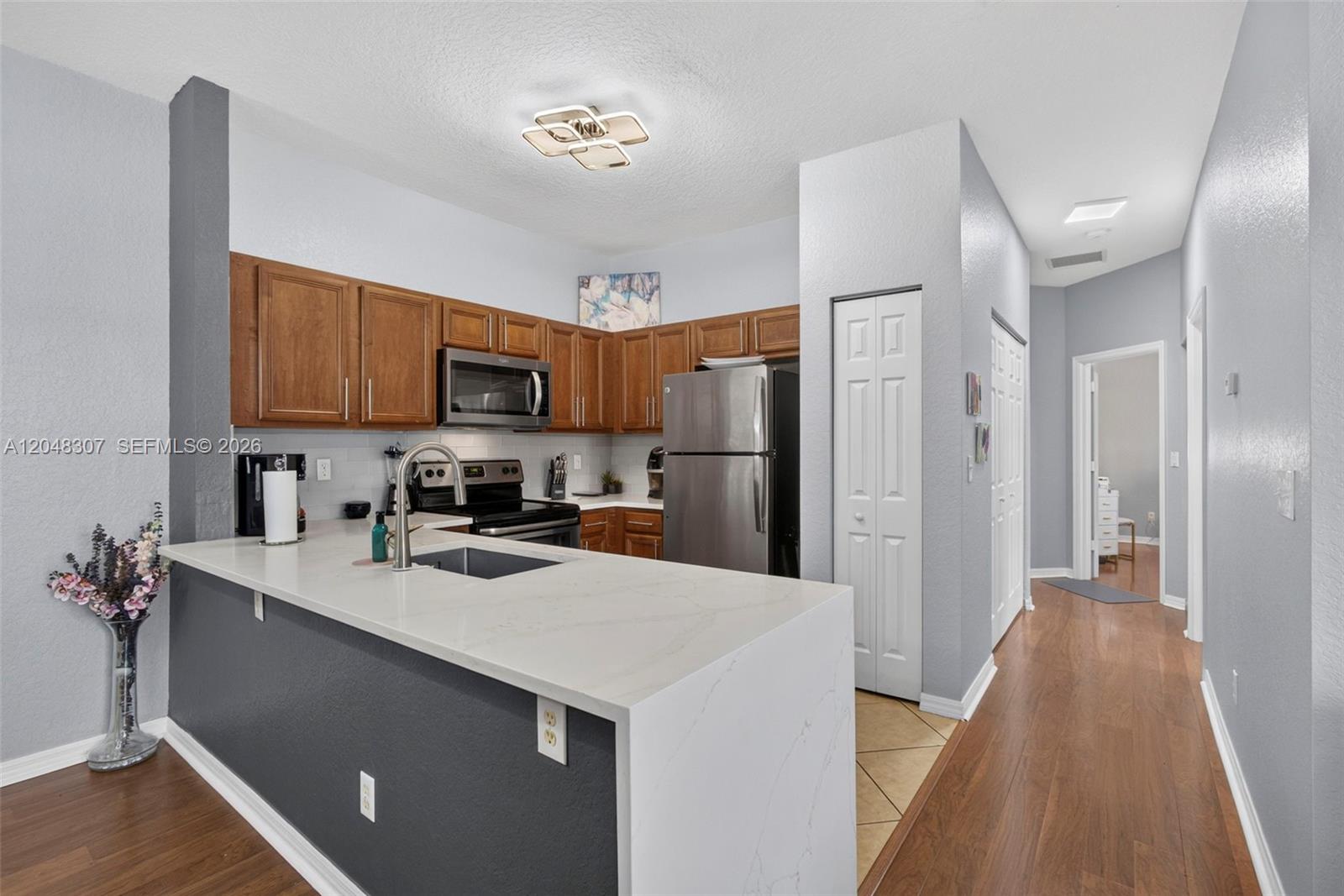 A kitchen features wood cabinets, stainless steel appliances, and a white quartz-topped peninsula island — 3107 Grandiflora Dr, Green Acres FL 33467, GREEN ACRES, FL