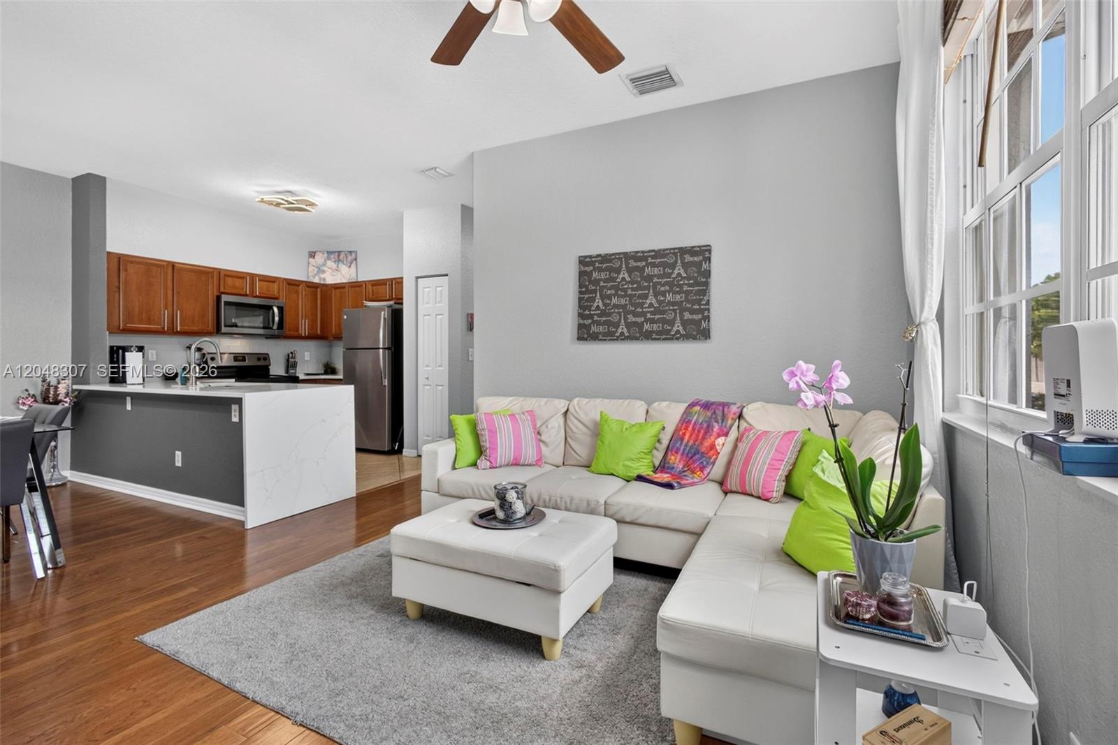A living room with a white sectional sofa and ottoman opens to a modern kitchen — 3107 Grandiflora Dr, Green Acres FL 33467, GREEN ACRES, FL