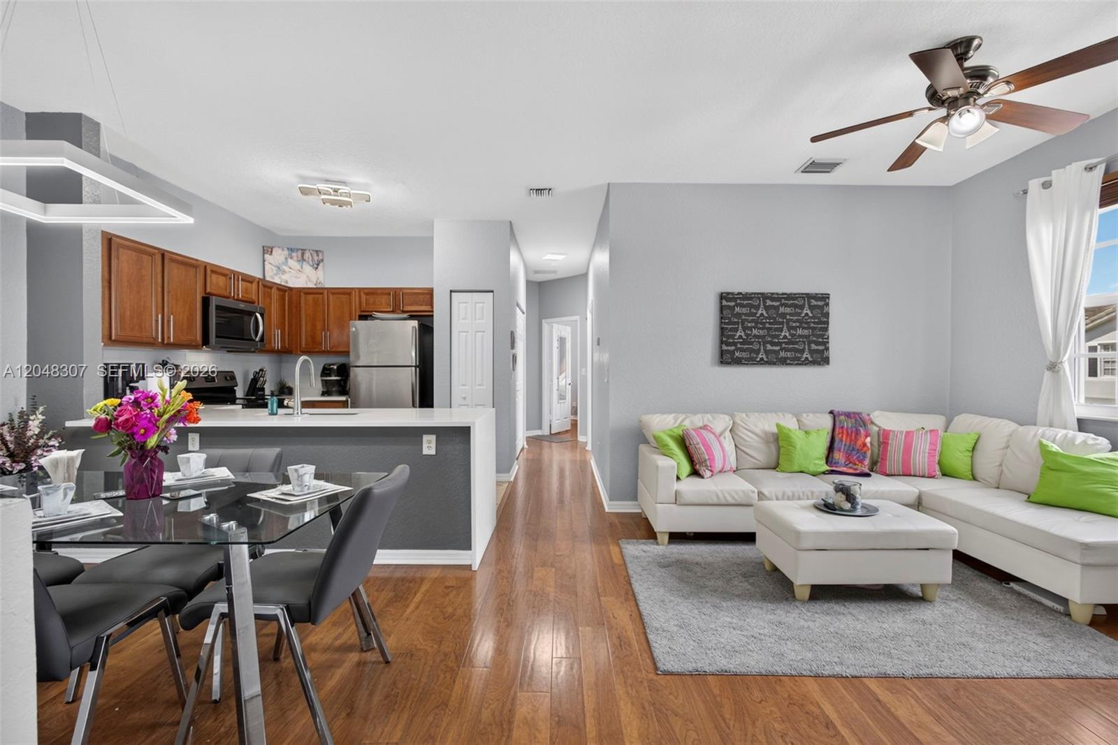 An open-concept living room and kitchen featuring wood flooring, white cabinetry, and a sectional sofa — 3107 Grandiflora Dr, Green Acres FL 33467, GREEN ACRES, FL