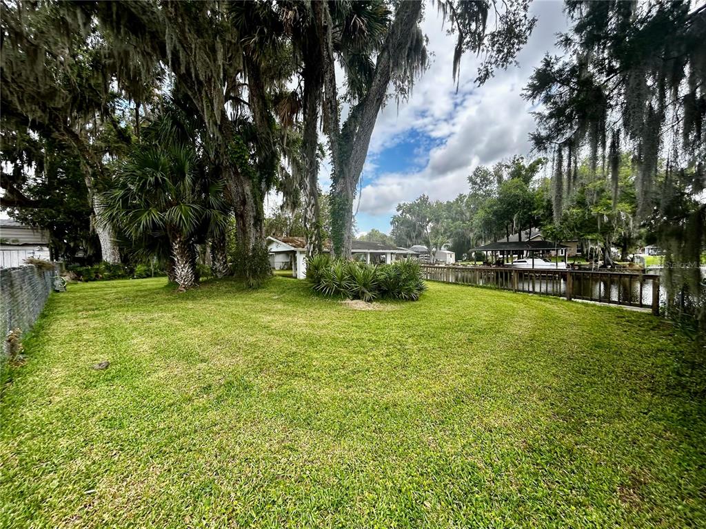 A grassy backyard features large oak trees, a wooden fence, and a boat dock — 2950 N SHELL ROAD, DELAND, FL