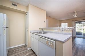 A kitchen with light-colored cabinets, a dishwasher, and a view into the living area — 5136 PARK CENTRAL DRIVE UNIT 215, ORLANDO, FL