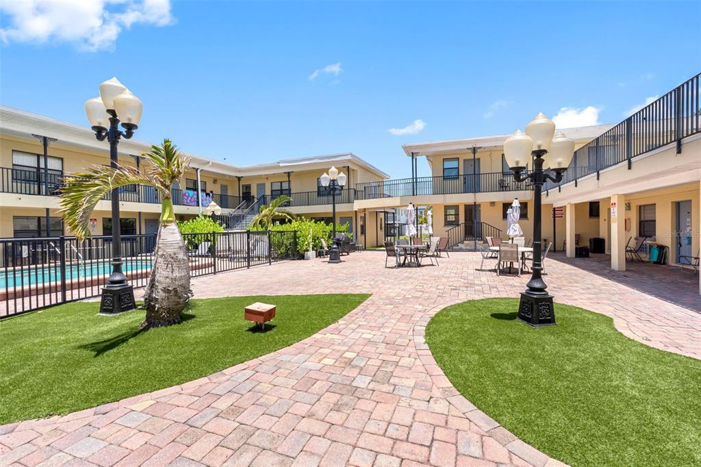 An outdoor courtyard with brick pavers, artificial turf, patio furniture, and two ornate lamp posts — 16333 GULF BOULEVARD UNIT 210, ST PETERSBURG, FL