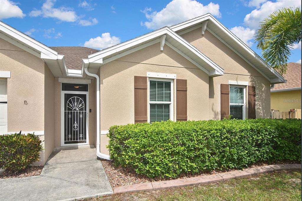 A beige house exterior features a front door with a decorative screen and green hedges — 7132 MIKASA DRIVE, PUNTA GORDA, FL
