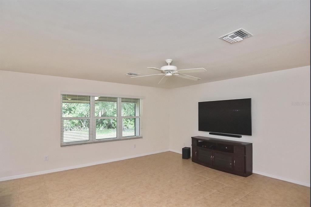 A living room with tile flooring, a ceiling fan, a large television, and a window — 7132 MIKASA DRIVE, PUNTA GORDA, FL