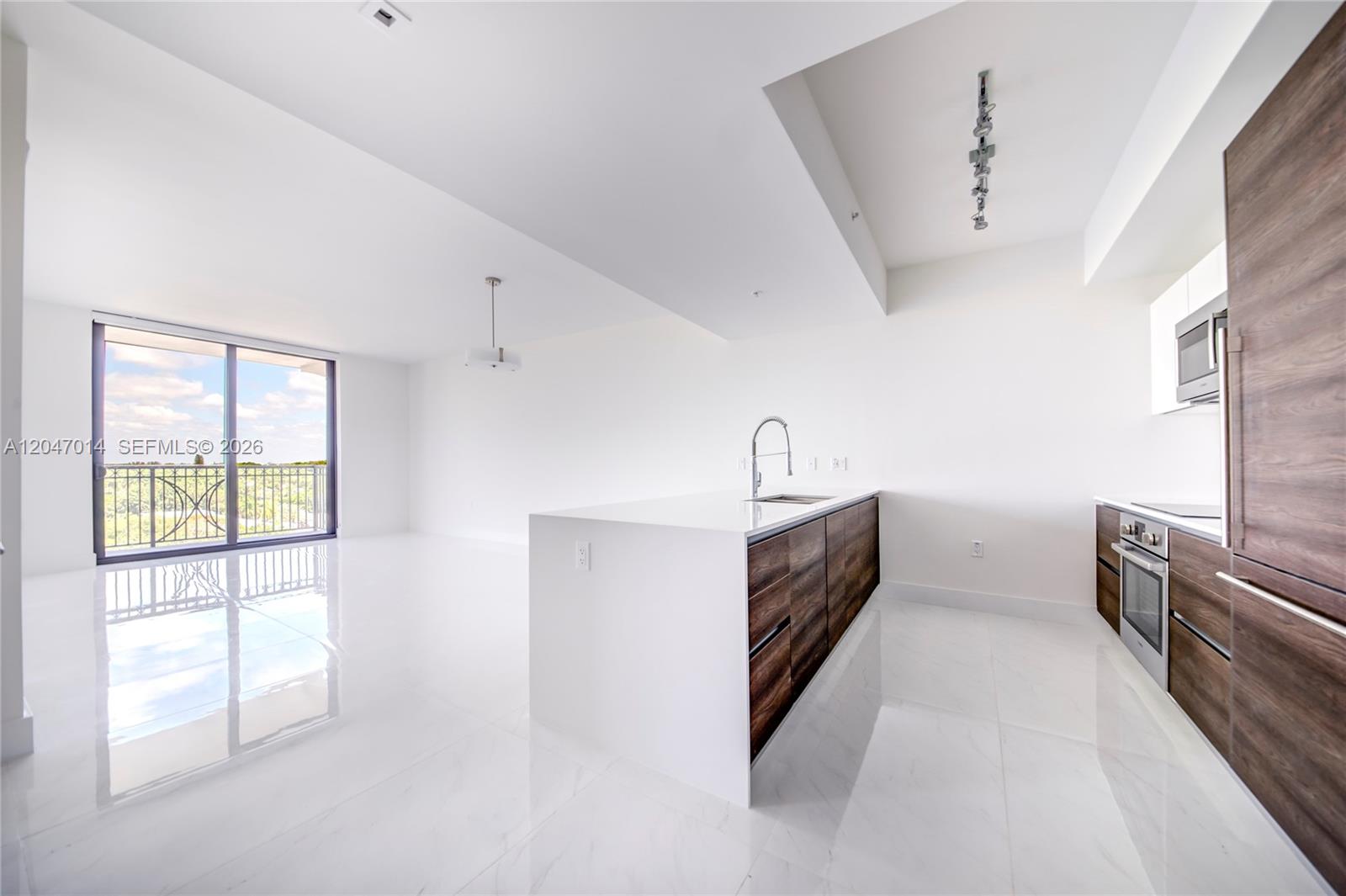 A modern kitchen with wood-toned cabinetry and a white island sits in an open-concept room — 301 Altara Ave # 733, Coral Gables FL 33146, CORAL GABLES, FL