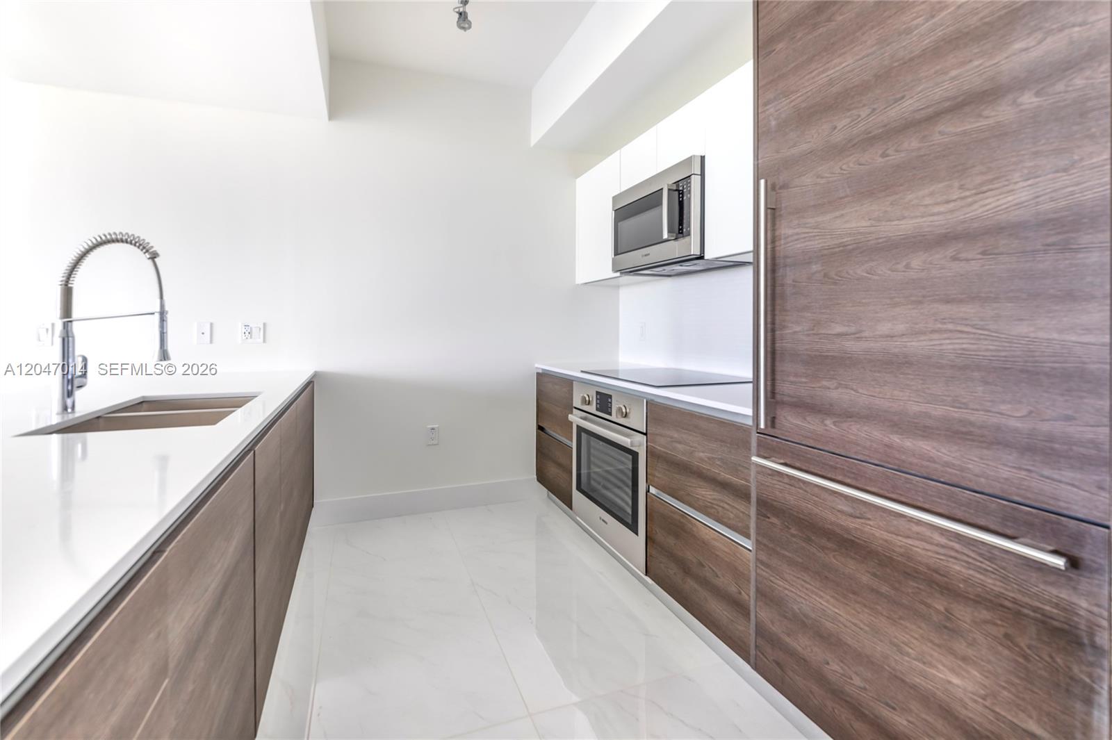 A modern galley kitchen features wood-grain cabinetry, white countertops, stainless steel appliances, and tile flooring — 301 Altara Ave # 733, Coral Gables FL 33146, CORAL GABLES, FL