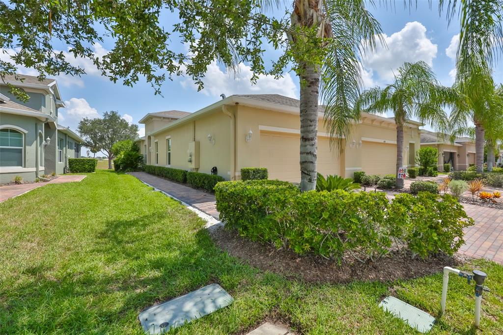 A tan house with a multi-car garage, a paved driveway, and manicured landscaping — 606 CHIPPER DRIVE, SUN CITY CENTER, FL