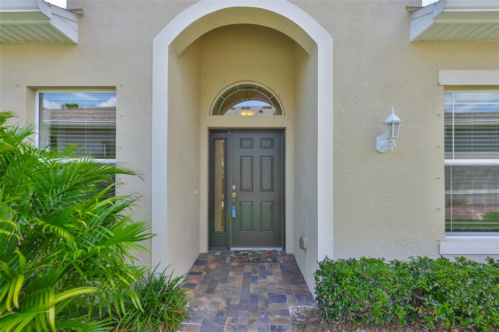 A front entryway features a dark door with a sidelight, arched transom, and brick walkway — 606 CHIPPER DRIVE, SUN CITY CENTER, FL