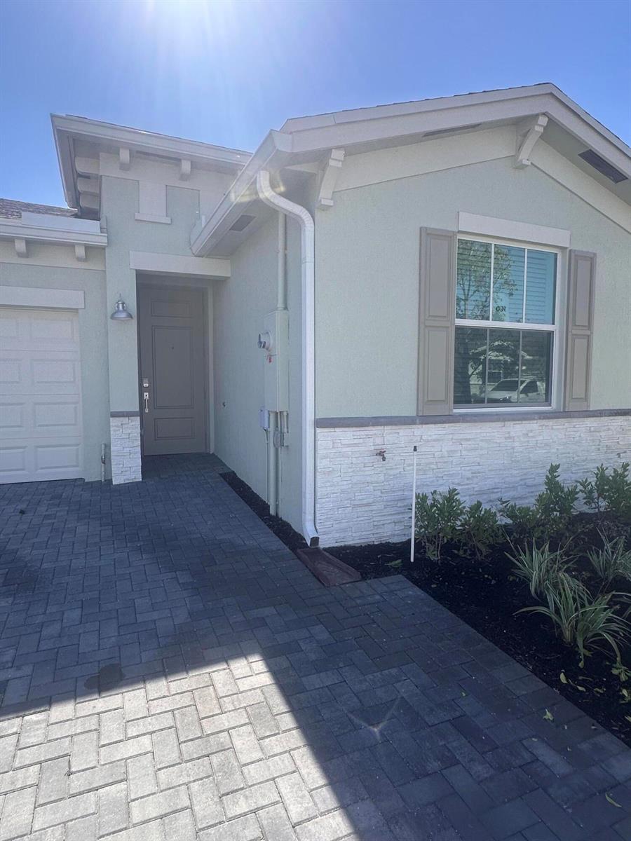 The exterior of a light green house features a stone veneer base and a paver driveway — 13776 Hero Path, Delray Beach FL 33484, DELRAY BEACH, FL