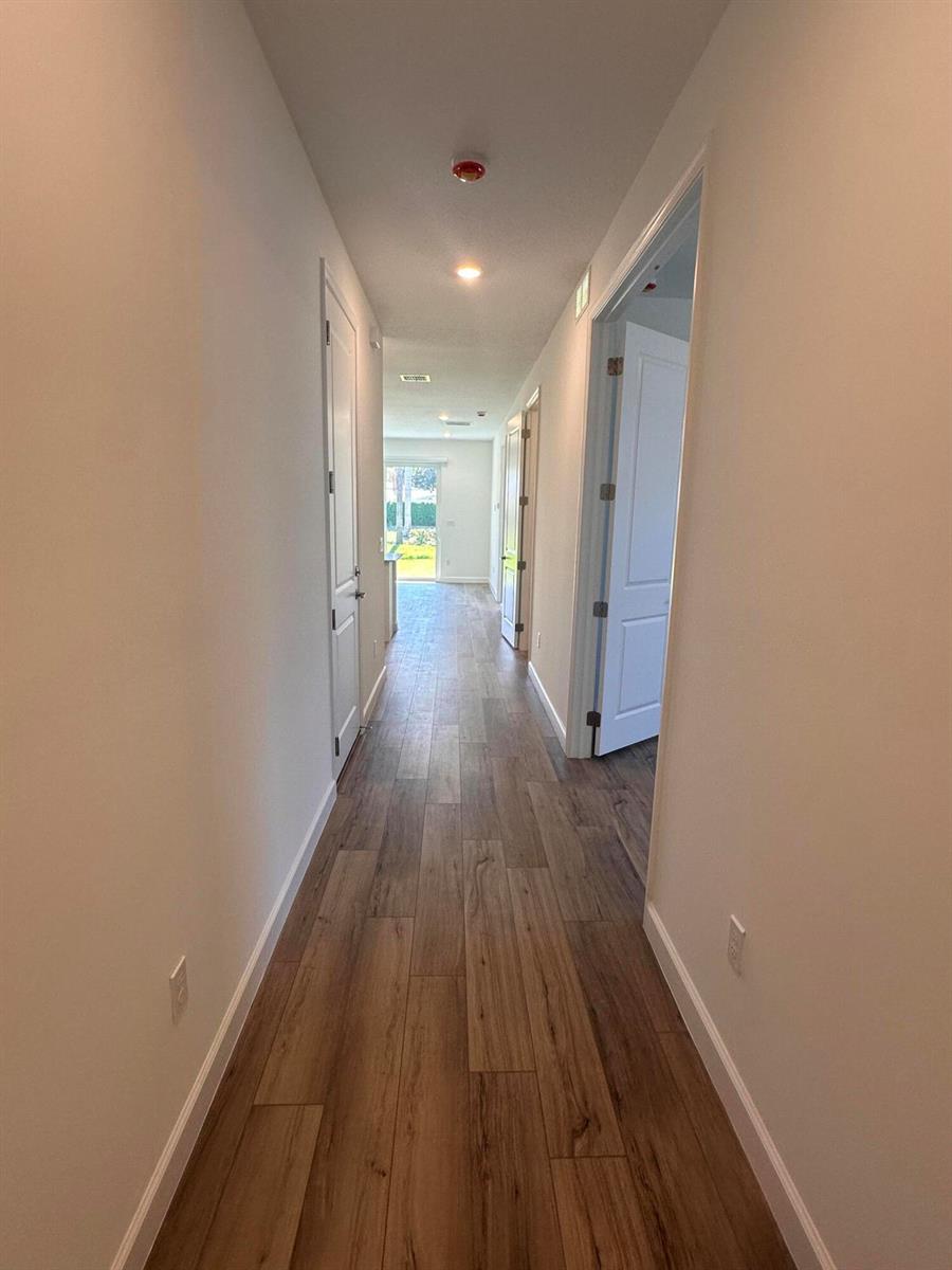 A long hallway with wood-look flooring leads toward a glass door at the end — 13776 Hero Path, Delray Beach FL 33484, DELRAY BEACH, FL