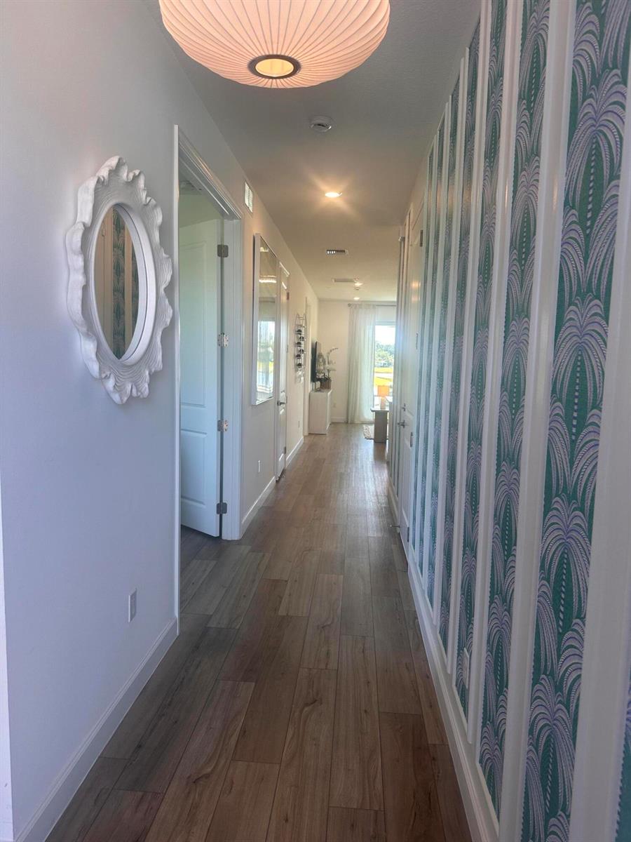 A hallway features wood-look flooring, a patterned wallpaper accent wall, and a white framed mirror — 13776 Hero Path, Delray Beach FL 33484, DELRAY BEACH, FL