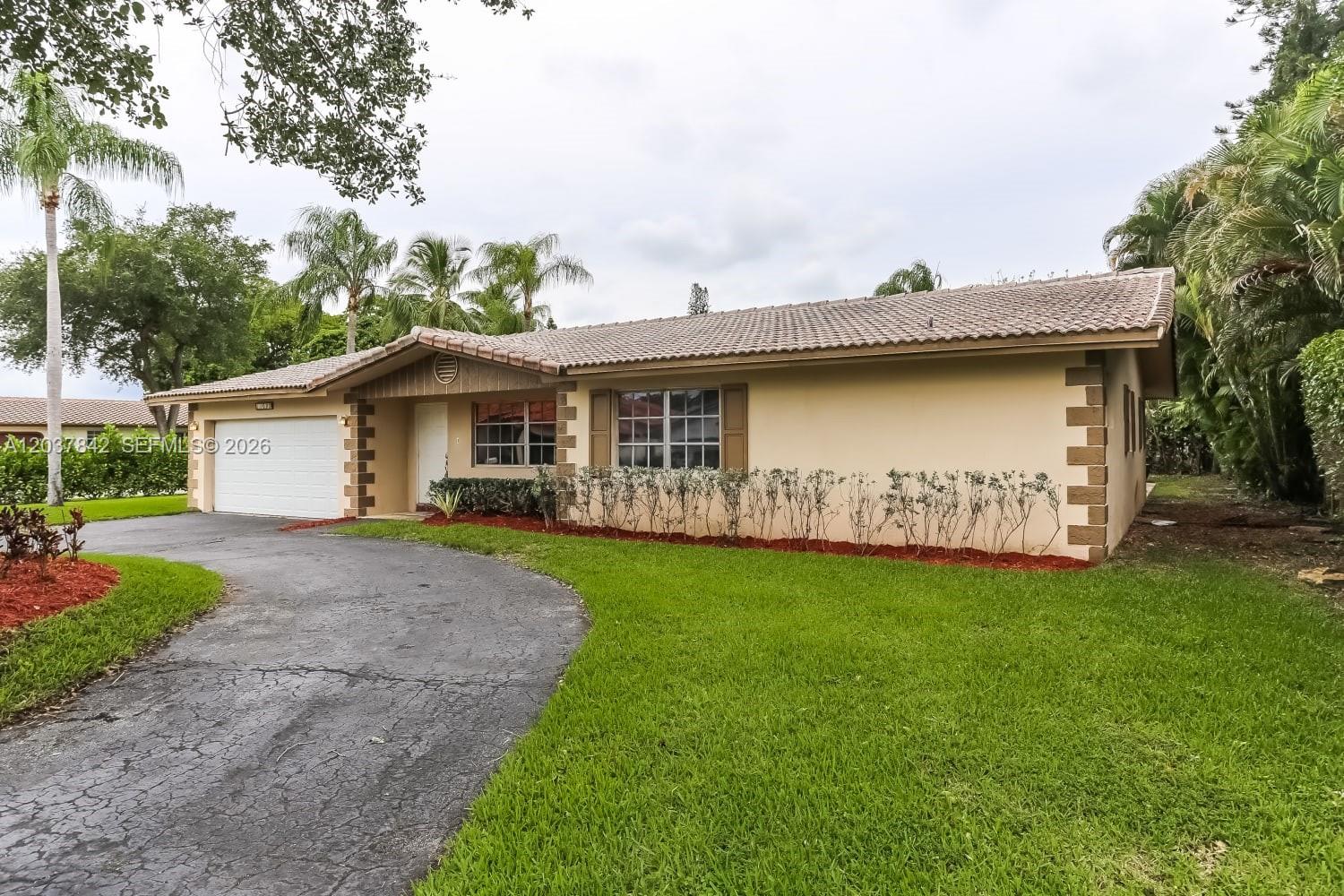 A single-story house with a tan stucco exterior, a tiled roof, and a paved driveway — CORAL SPRINGS, FL
