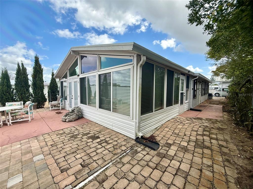 A white mobile home features a sunroom with large windows and a paver patio — 205 PANSY STREET, DAVENPORT, FL
