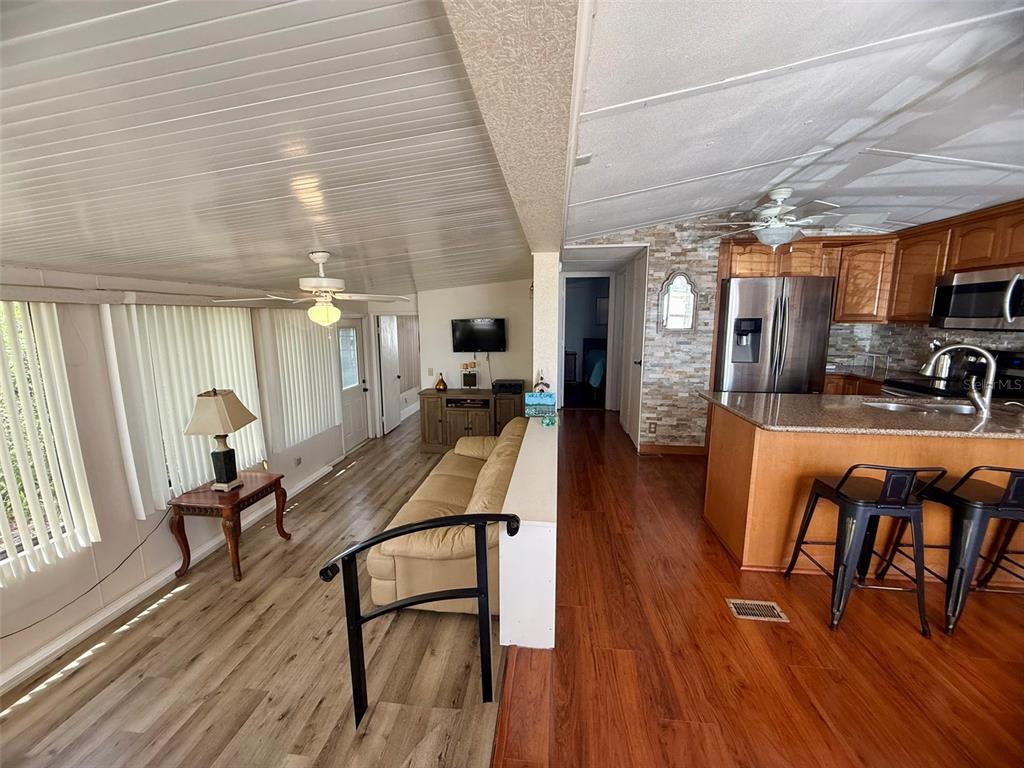 An open-concept living room and kitchen featuring wood-look flooring and a stone-tiled accent wall — 205 PANSY STREET, DAVENPORT, FL