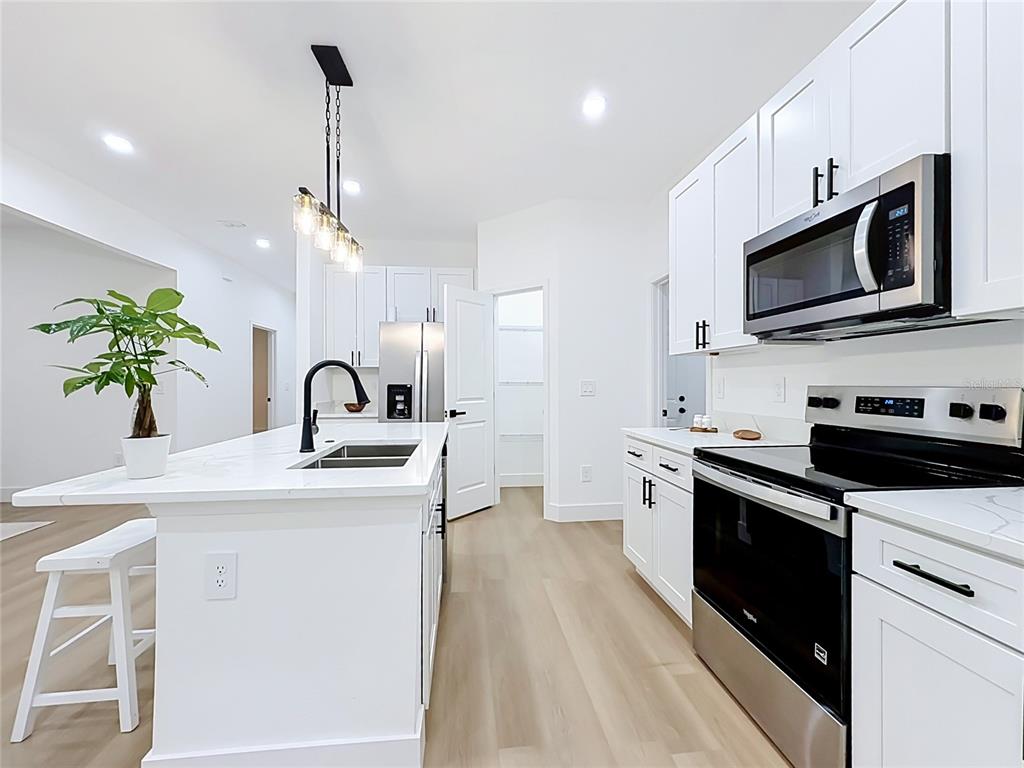 A modern white kitchen features a center island with a sink and stainless steel appliances — 7107 BLEDSOE AVENUE, ORLANDO, FL