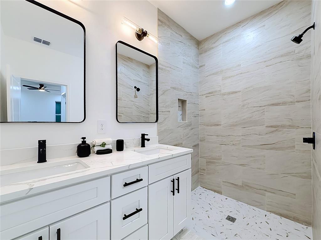 A modern bathroom features a double vanity with black fixtures and a walk-in tiled shower — 7107 BLEDSOE AVENUE, ORLANDO, FL
