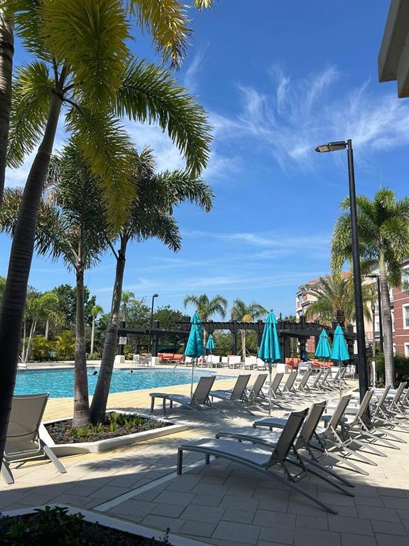 A swimming pool area features lounge chairs, blue umbrellas, and palm trees under a blue sky — 4804 CAYVIEW AVENUE UNIT 20412, ORLANDO, FL