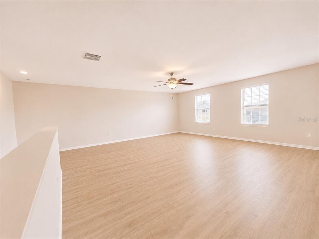 An empty, spacious room features light wood-look flooring, beige walls, and a ceiling fan — 5462 GRAYS HARBOR COURT, WIMAUMA, FL