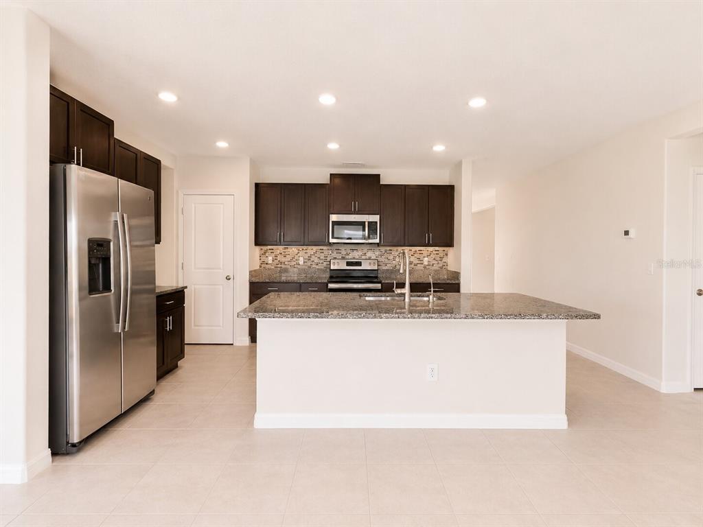 A kitchen with dark wood cabinets, granite countertops, a stainless steel refrigerator, and an island — 5462 GRAYS HARBOR COURT, WIMAUMA, FL
