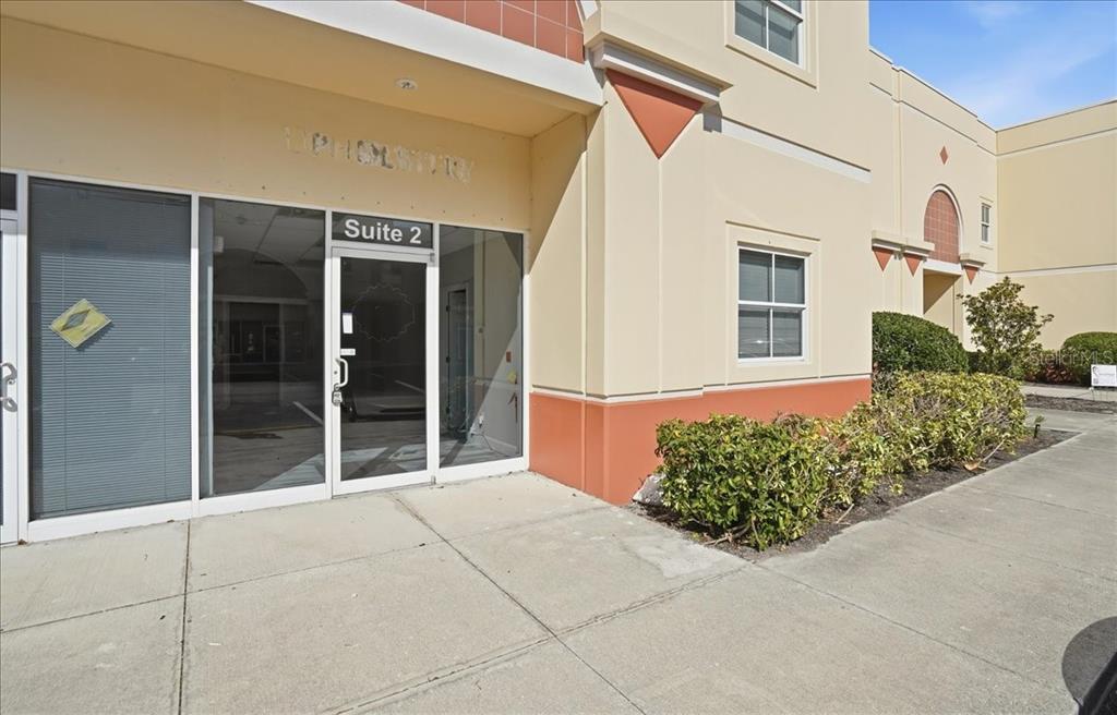 The exterior of a commercial building features a glass entrance door labeled Suite 2 — 6321 PORTER UNIT 2, SARASOTA, FL