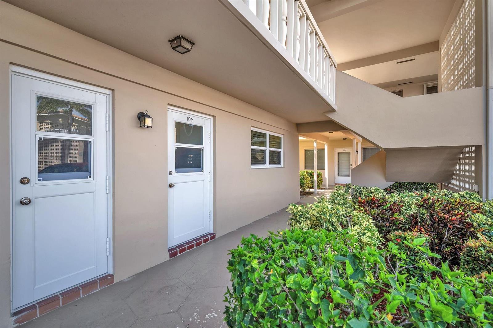 A ground-level apartment exterior features a white door labeled 104, stairs, and landscaping — 2131 NE 42nd Court # 104e, Lighthouse Point FL 33064, LIGHTHOUSE POINT, FL