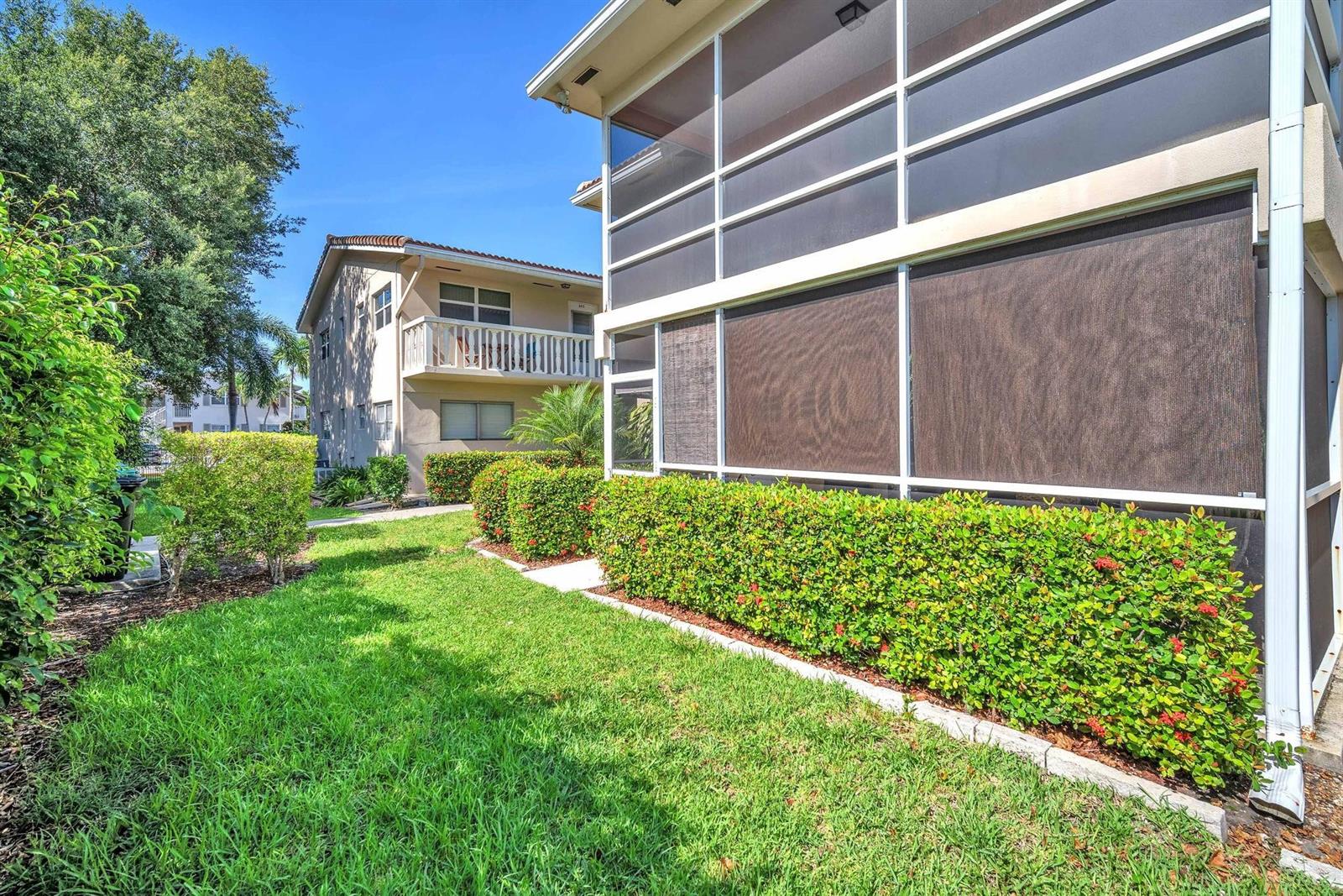 A view of a grassy yard with manicured hedges and a screened-in patio area — 2131 NE 42nd Court # 104e, Lighthouse Point FL 33064, LIGHTHOUSE POINT, FL