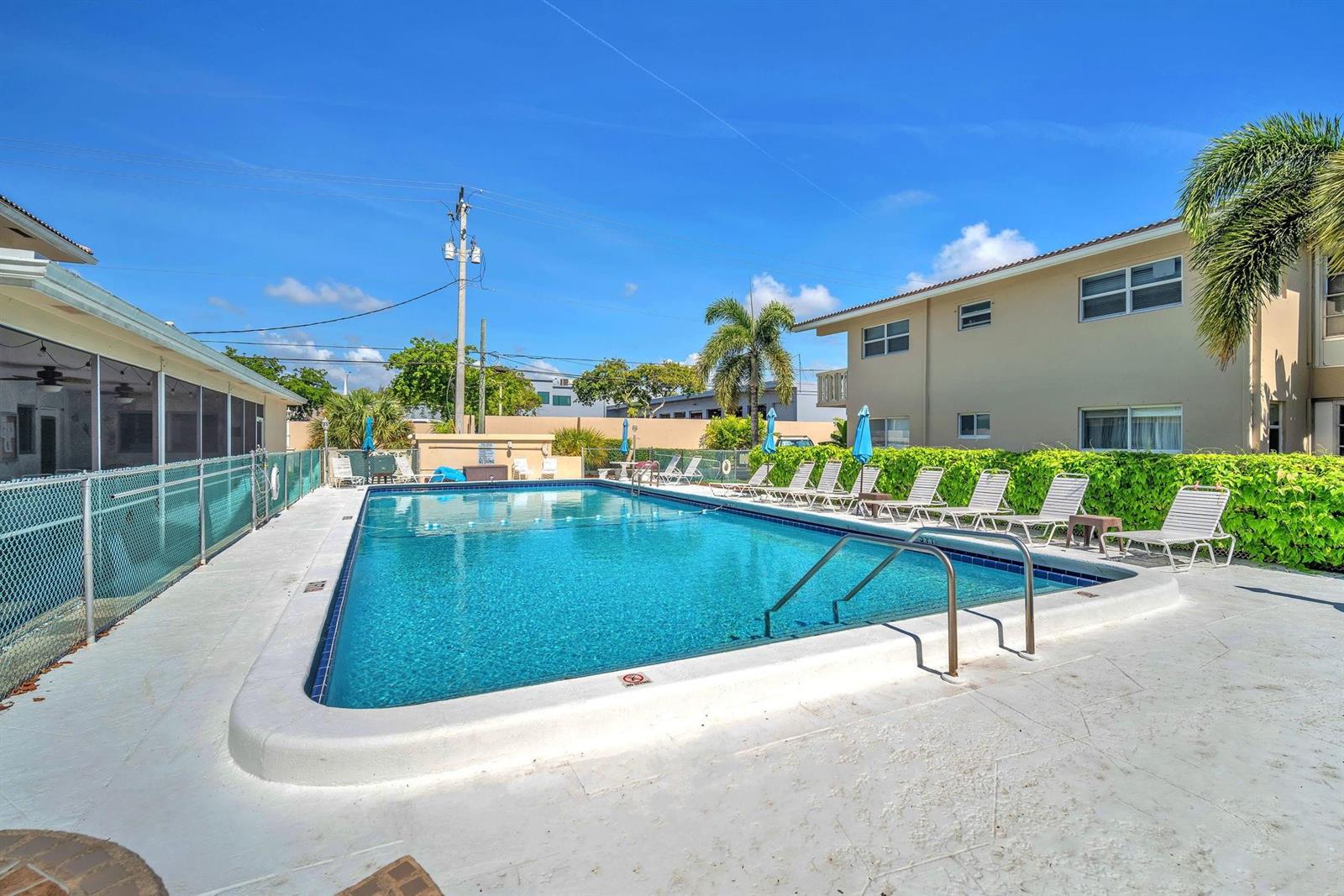 An outdoor swimming pool surrounded by lounge chairs and a building under a blue sky — 2131 NE 42nd Court # 104e, Lighthouse Point FL 33064, LIGHTHOUSE POINT, FL