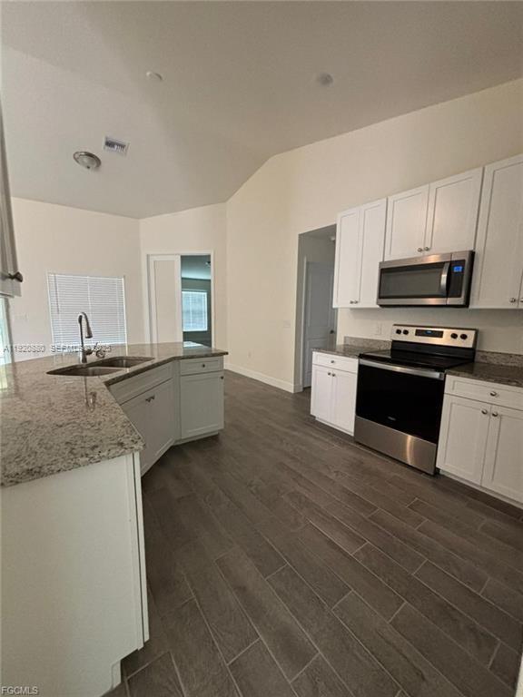 A kitchen features white cabinets, granite countertops, stainless steel appliances, and gray wood-look tile flooring — 2614 27th ST W, Lehigh Acres FL 33971, LEHIGH ACRES, FL