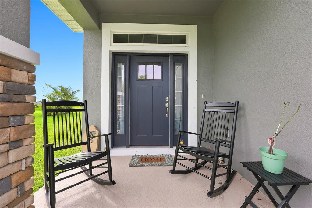 A covered front porch features two black rocking chairs, a small table, and a dark door — 16331 66TH LANE E, PARRISH, FL