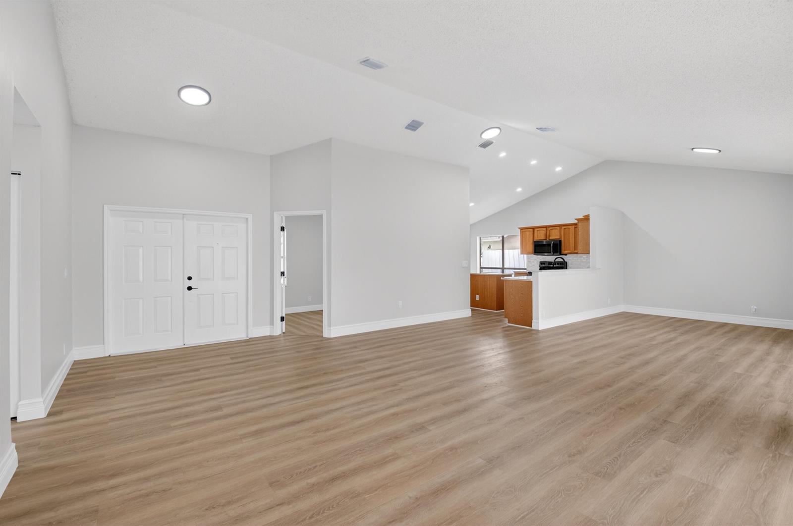 An open-concept living area features light wood-look flooring, vaulted ceilings, and an adjacent kitchen — 9537 Majestic Way, Boynton Beach FL 33437, BOYNTON BEACH, FL