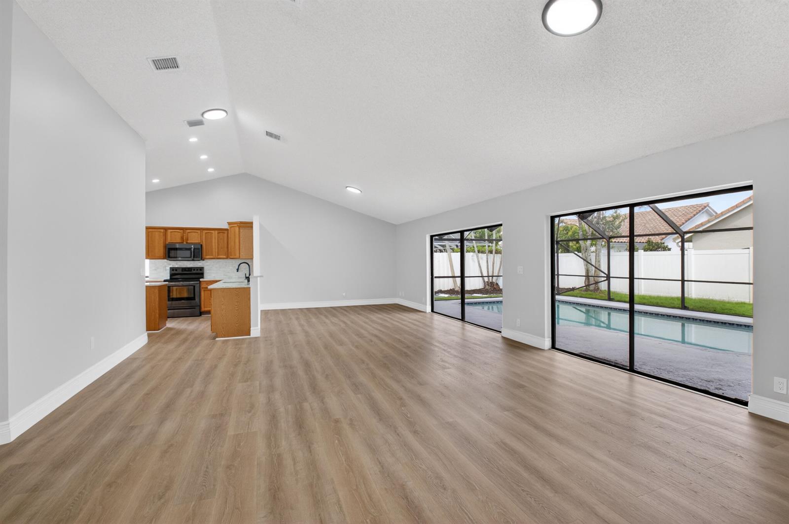 An open-concept living area features light wood-look flooring, vaulted ceilings, and sliding glass doors — 9537 Majestic Way, Boynton Beach FL 33437, BOYNTON BEACH, FL