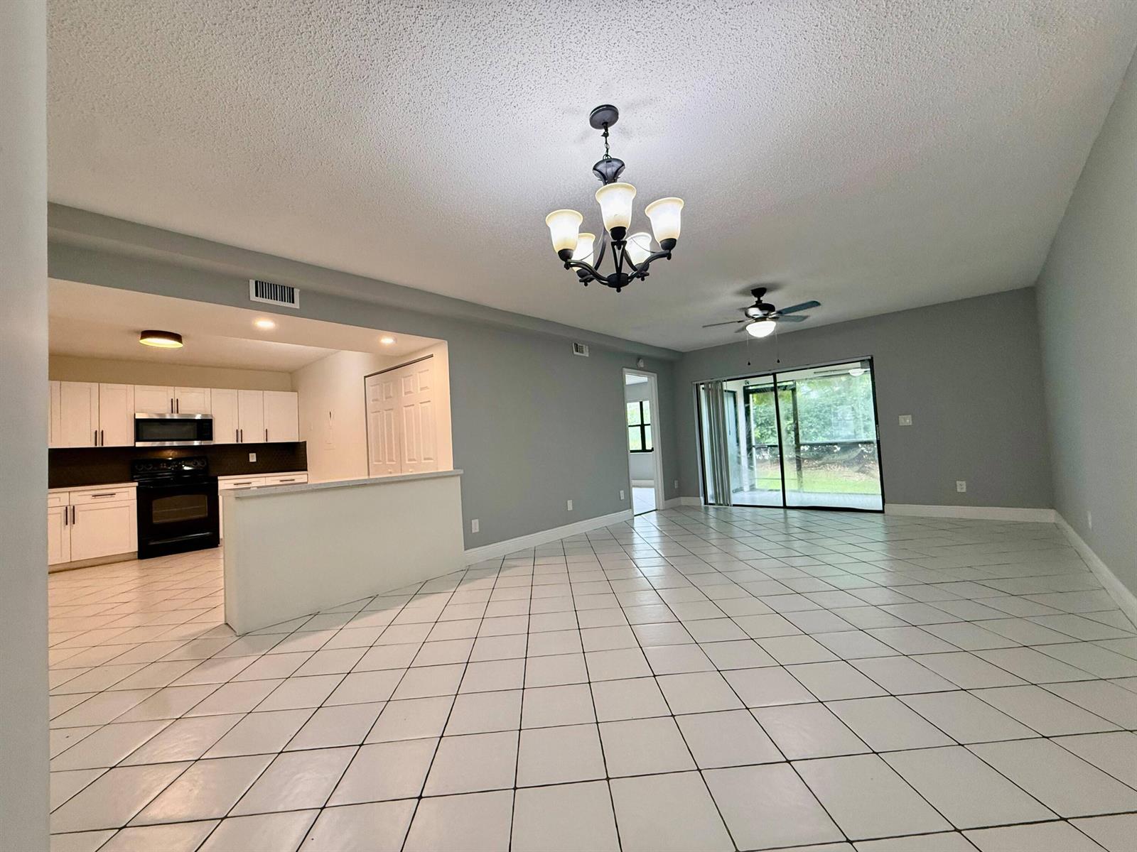 An open-concept living and dining area with white tile floors, a kitchen, and sliding doors — 9633 Riverside Drive # E2, Coral Springs FL 33071, CORAL SPRINGS, FL