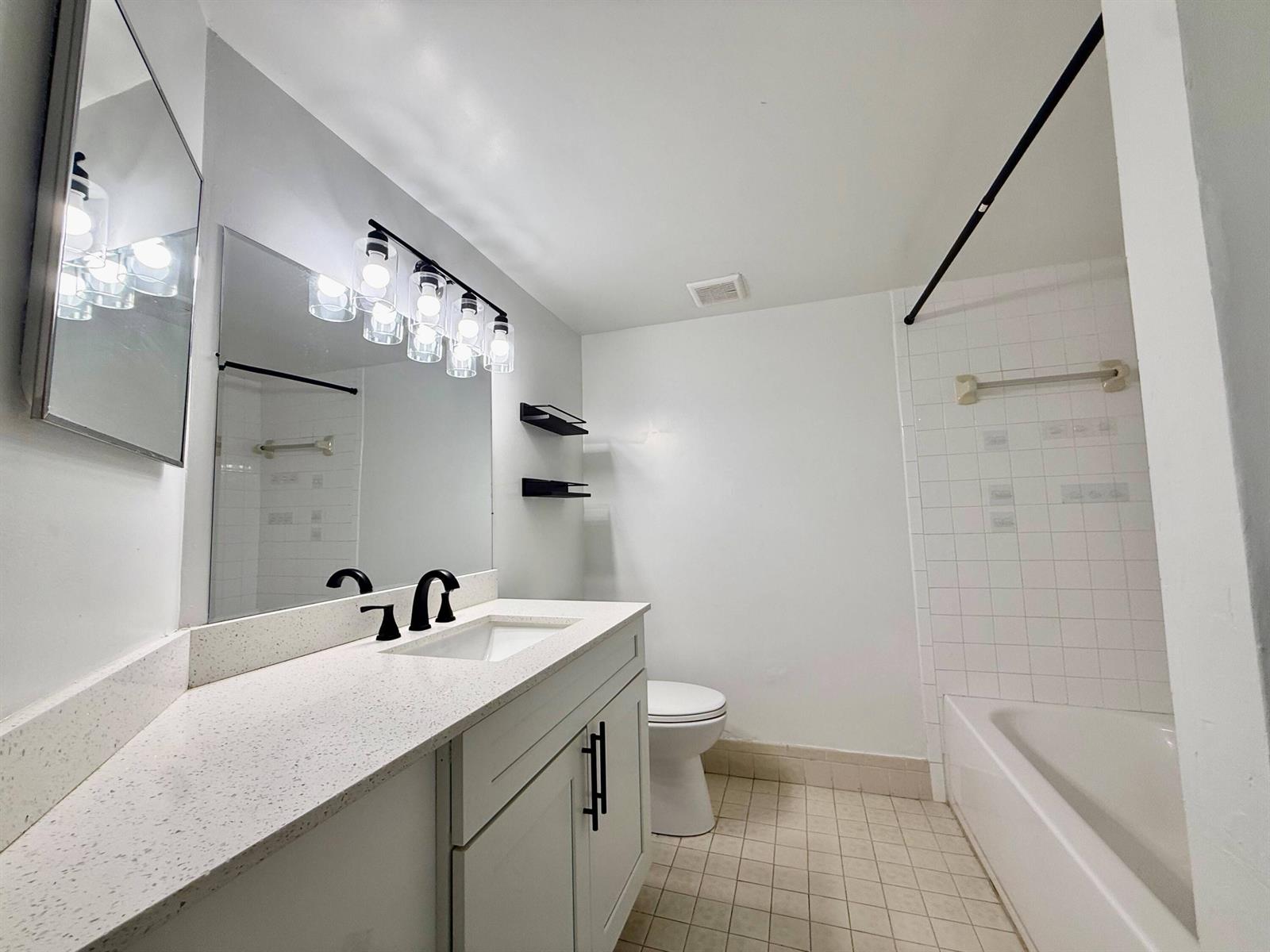 A bathroom features a white vanity with a speckled countertop, black fixtures, and a tub — 9633 Riverside Drive # E2, Coral Springs FL 33071, CORAL SPRINGS, FL