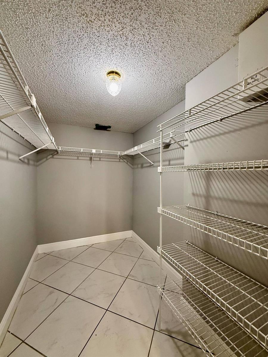 A walk-in closet with white wire shelving, gray walls, and light-colored tile flooring — 9633 Riverside Drive # E2, Coral Springs FL 33071, CORAL SPRINGS, FL