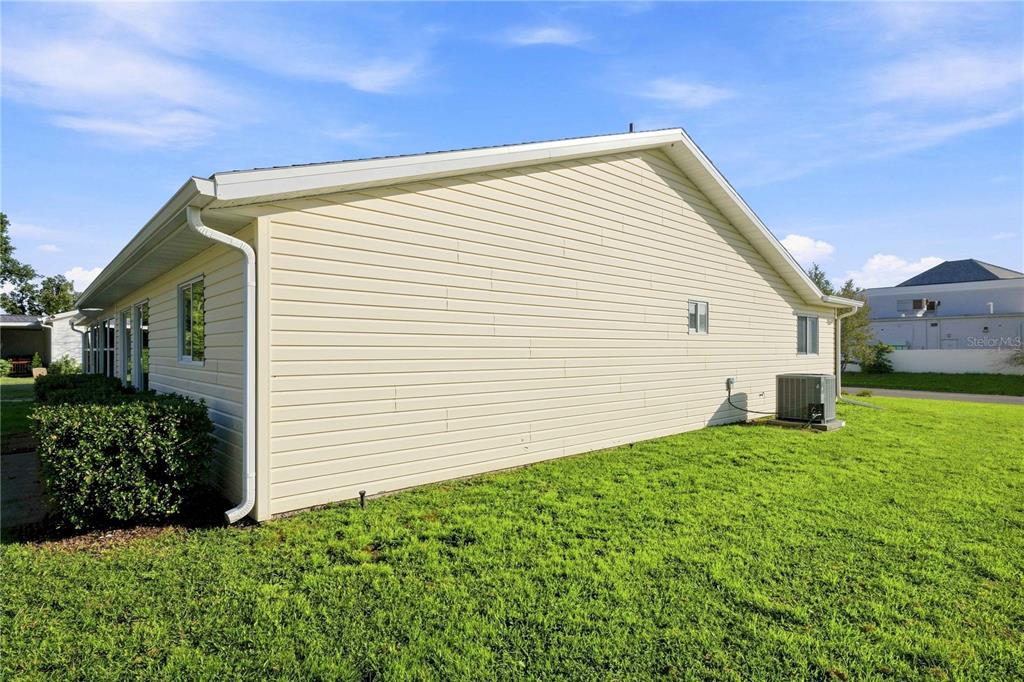 The side exterior of a light-colored vinyl-sided house with a central air conditioning unit — 17960 SE 108TH COURT, SUMMERFIELD, FL