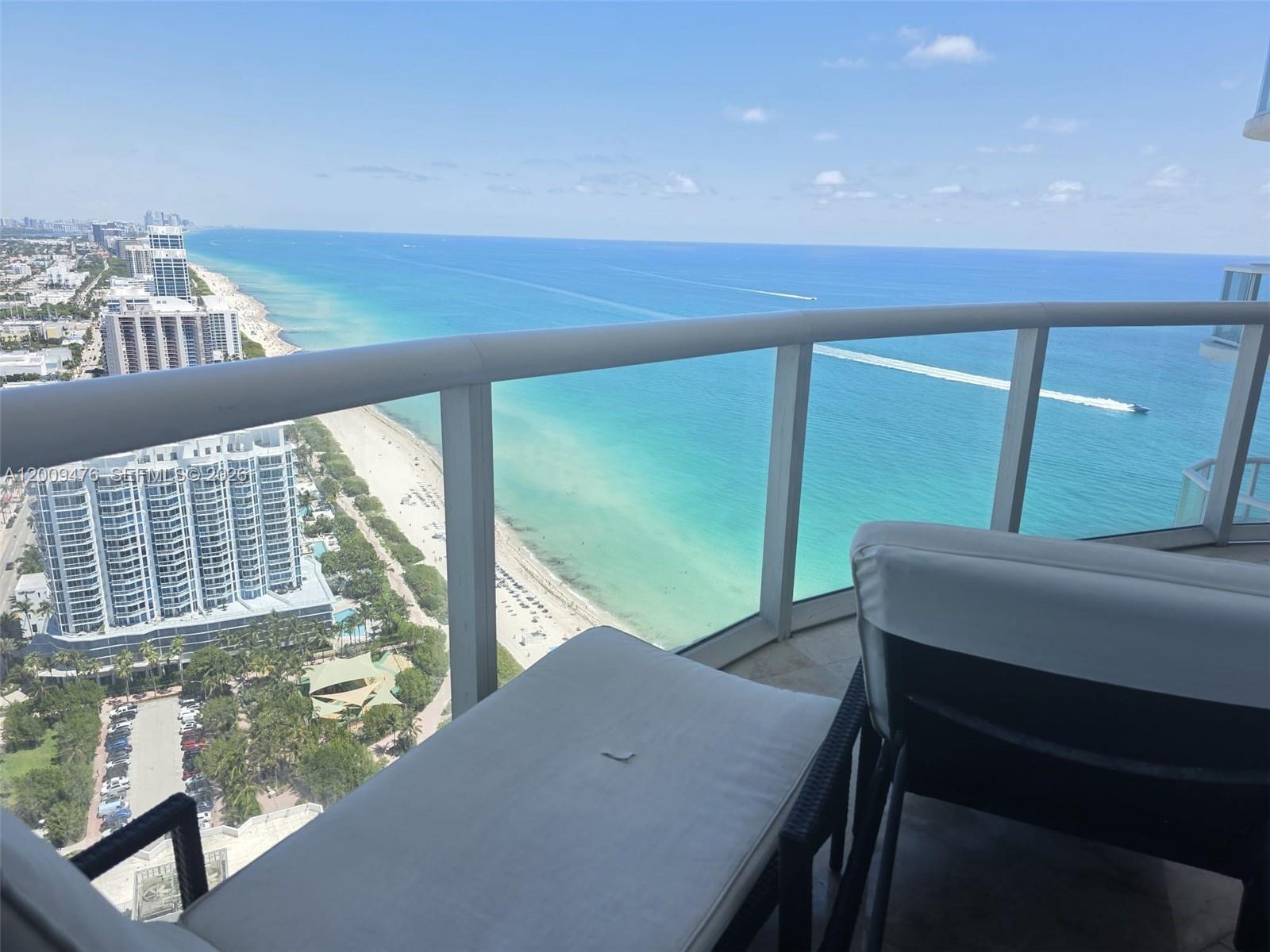 A high-rise balcony overlooks a sandy beach and the ocean with a boat passing by — 6365 Collins Ave # 4311, Miami Beach FL 33141, MIAMI BEACH, FL