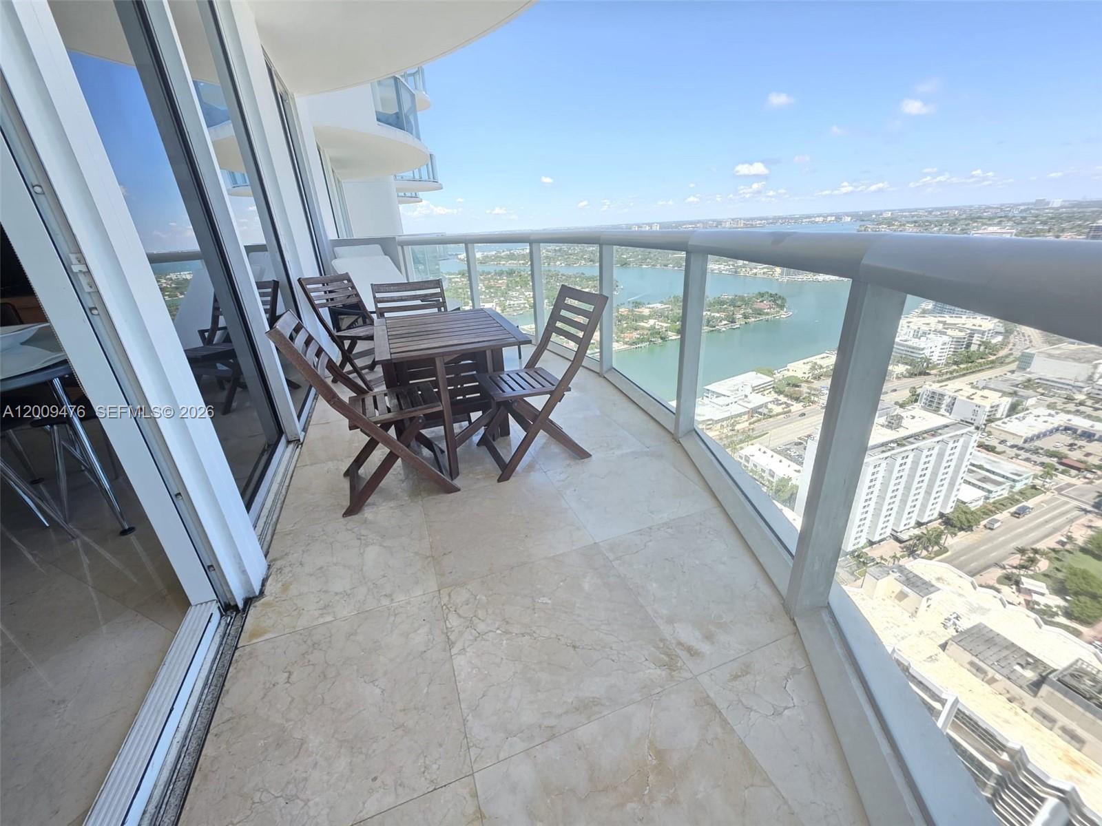 A balcony with a wooden table and chairs overlooks a coastal city and water — 6365 Collins Ave # 4311, Miami Beach FL 33141, MIAMI BEACH, FL