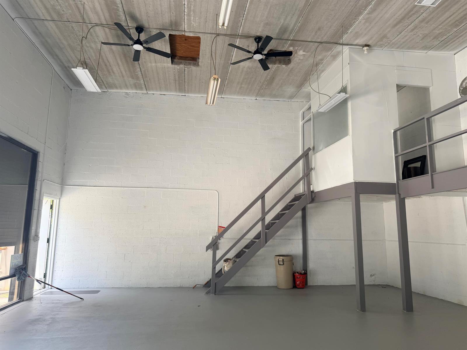 An industrial-style room features white block walls, a concrete ceiling, ceiling fans, and a staircase — 1791 Blount Road # 922, Pompano Beach FL 33069, POMPANO BEACH, FL