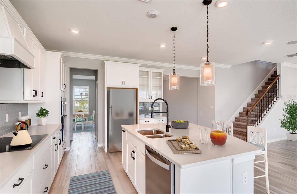A modern kitchen features white cabinetry, a large central island, and a staircase nearby — 5171 MOCKINGBIRD SOUND COURT, SANFORD, FL