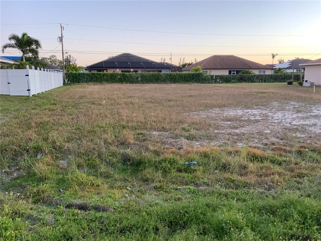 A vacant, grassy residential lot is bordered by a white fence and neighboring houses — 312 SE 19TH LANE, CAPE CORAL, FL