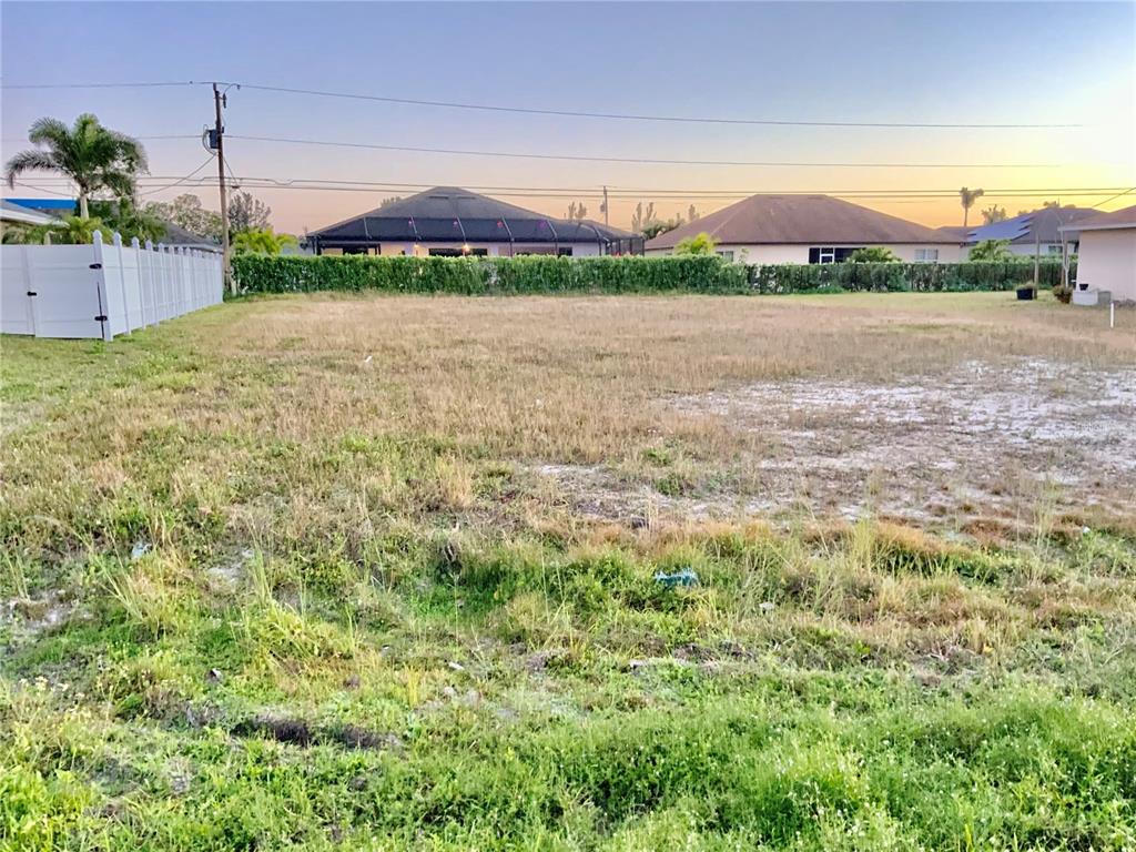 A vacant, grassy residential lot is bordered by a white fence and neighboring houses — 312 SE 19TH LANE, CAPE CORAL, FL