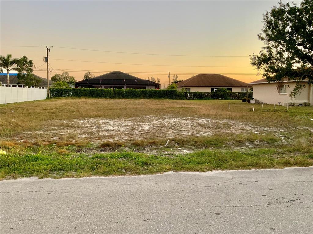 A vacant, grassy residential lot sits between two houses under a sunset sky — 312 SE 19TH LANE, CAPE CORAL, FL