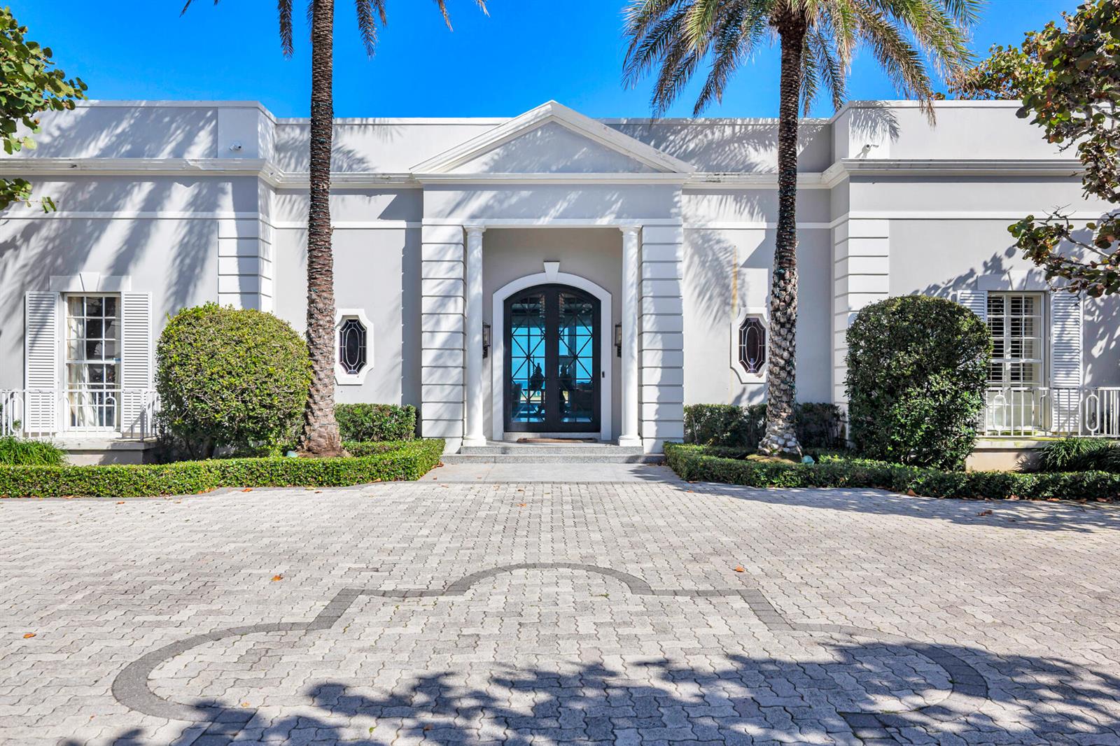 The exterior of a white neoclassical house features a paved driveway, palm trees, and columns — 5 Via Los Incas, Palm Beach FL 33480, PALM BEACH, FL