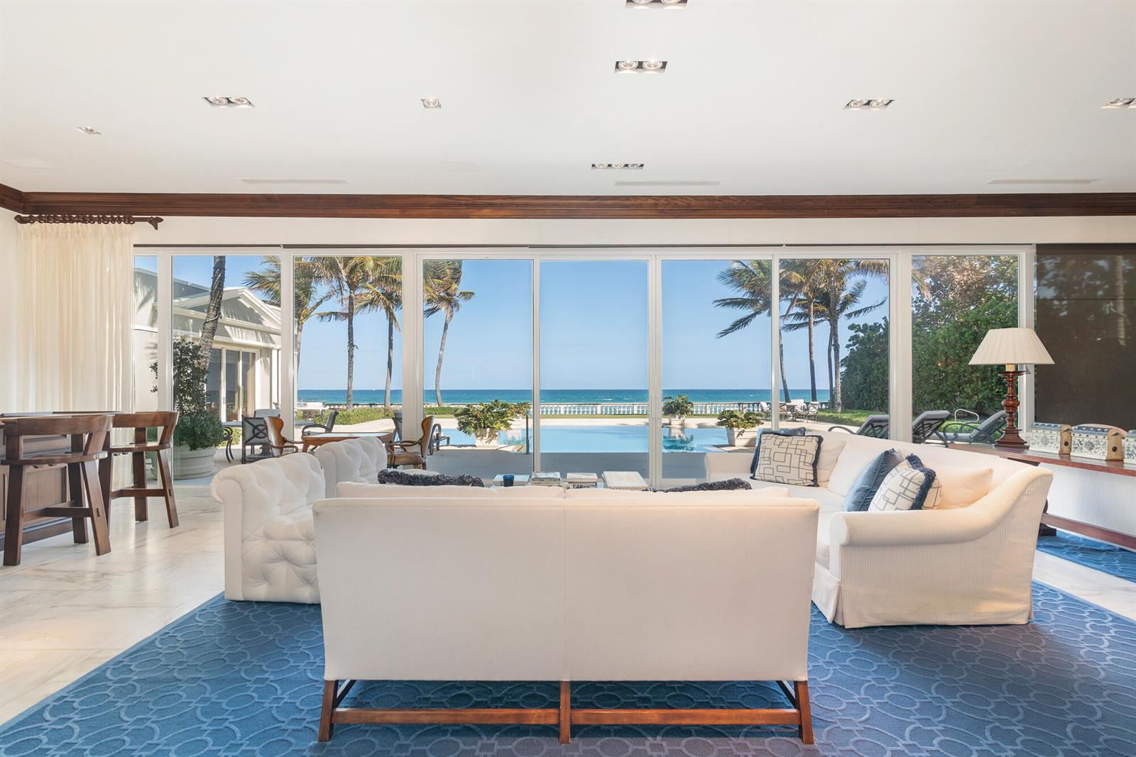 A living room with white sofas, a blue patterned rug, and floor-to-ceiling windows overlooking a pool — 5 Via Los Incas, Palm Beach FL 33480, PALM BEACH, FL