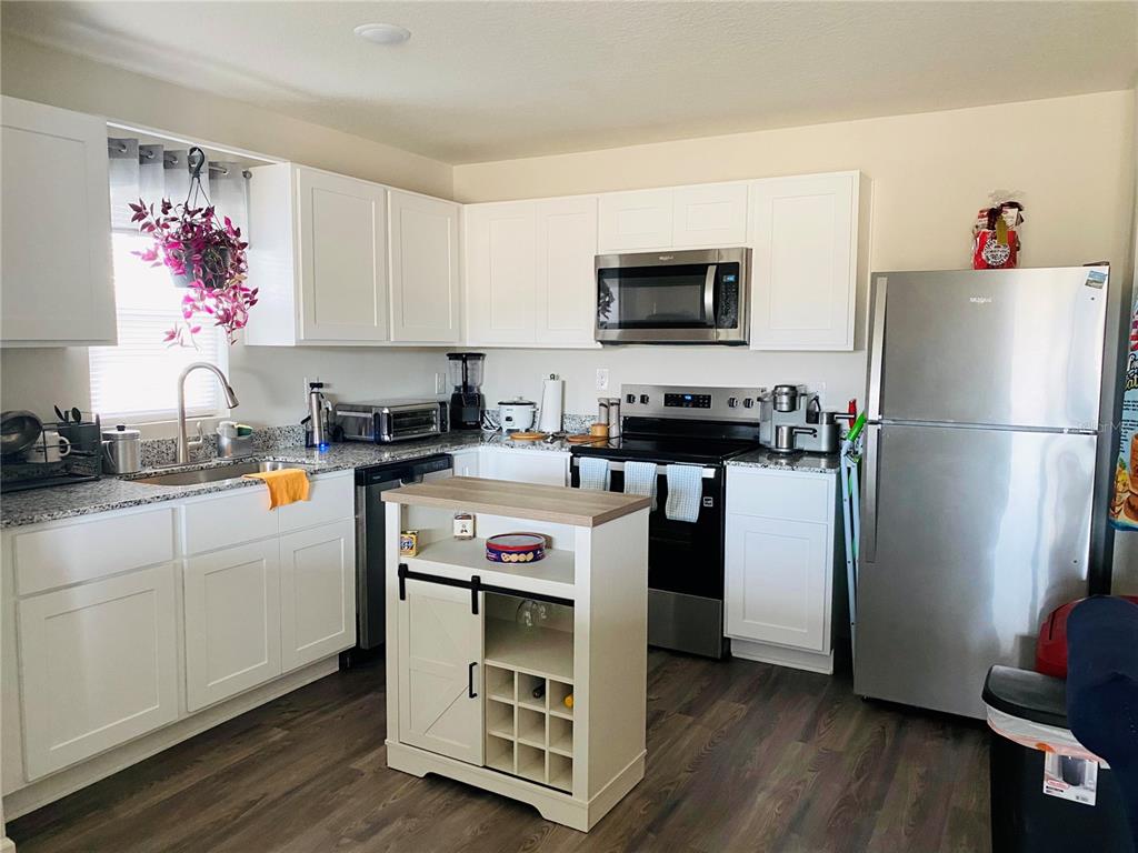 A kitchen features white cabinets, stainless steel appliances, granite countertops, and a central rolling island — 2295 NW 25TH LANE, OCALA, FL