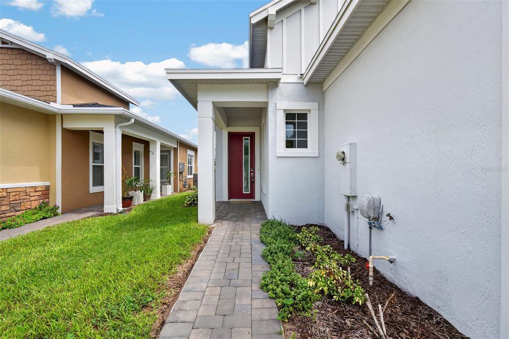 A paved walkway leads to a red front door between two suburban residential homes — 2286 DATURA LOOP, ST CLOUD, FL